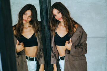 A woman in a stylish black jacket and beige pants joyfully holds a camera, capturing a moment in a sunlit room.