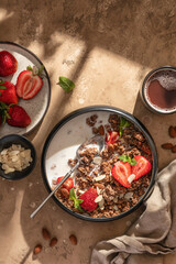 Healthy breakfast: fresh granola, muesli with milk, strawberry and almond for breakfast on brown textured background in bright morning light. Top view