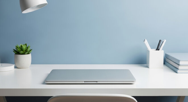 Minimalist modern workspace with closed laptop, succulent plant and office supplies on white desk against soft blue wall, clean organized home office for productivity and focus