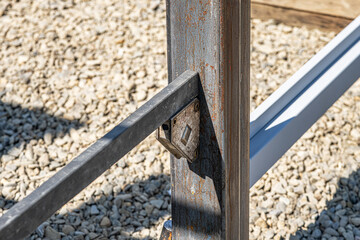 Close-up of a rusty metal corner bracket connecting a steel beam to a vertical post on a gravel...