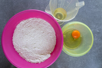 flour, cracked egg, and oil prepared for baking on grey background