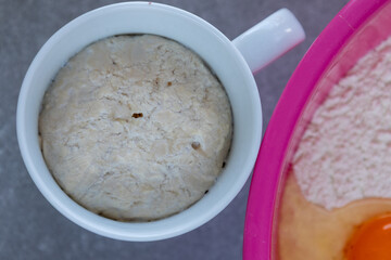 yeast in a mug and flour with egg in a bowl on grey background