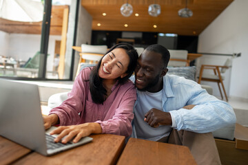Young happy multiethnic couple having fun while using laptop at home. Happy couple discussing future