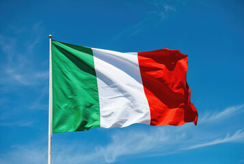 Italian flag waves in clear blue sky with wispy clouds. Green, white, and red vertical bands fill the frame. Symbol of Italy, national pride, and patriotism. Bright sunny day.