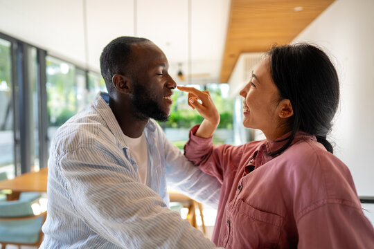 Excited child-free multiethnic couple embracing and laughing in modern living room, calm lifestyle - Powered by Adobe