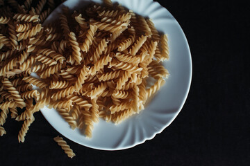 Raw Fusilli Pasta on White Plate with Black Background