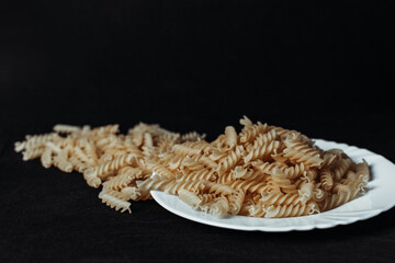 Raw Fusilli Pasta on White Plate with Black Background