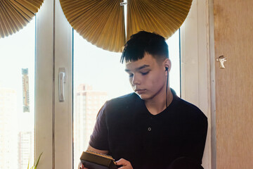 Young person holds a kalimba near a window, bathed in sunlight. Close-up portrait showcasing music and instrument.