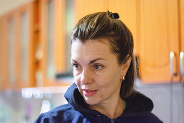 Portrait of young woman in blue hoodie looking at camera with slight smile in bright kitchen interior with warm lighting and blurred background