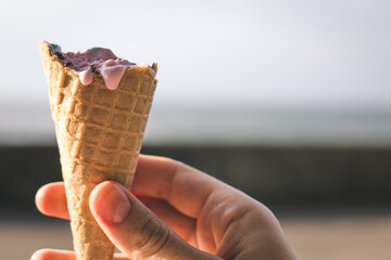 A delicious ice cream cone melts on a warm summer day. A hand holds a melting ice cream cone, with...