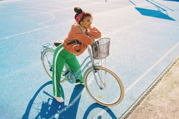 Outdoor fashion portrait of pretty african woman leaning on the bike
