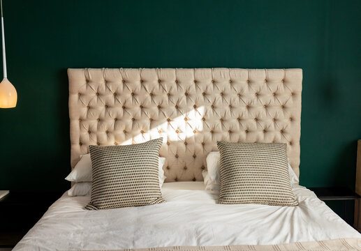 Bed is sitting under hanging lamp with tufted headboard, white bedding and geometric pillows
