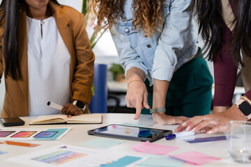 Diverse female colleagues collaborating over digital tablet and color printouts in office workspace