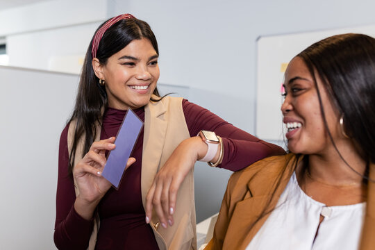 Diverse female colleagues discussing design ideas at cubicle with color swatch and smartwatch