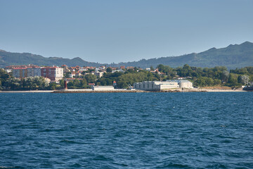 Photograph of the lighthouse next to the Museum do Mar in Vigo with modern design buildings surrounded by trees and the Atlantic coast