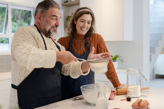 Couple using fine mesh strainer to sift flour into glass mixing bowl at modern kitchen island