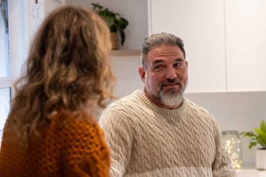 Couple wearing knit sweaters talking at home kitchen counter with potted plant and string lights