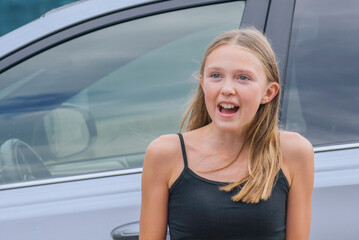 Young girl expresses excitement while standing by a car in a casual outdoor setting during daytime