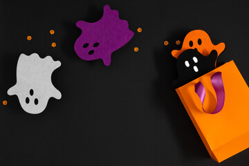 Cute Halloween themed composition with orange gift bag and bright colored ghosts on black...