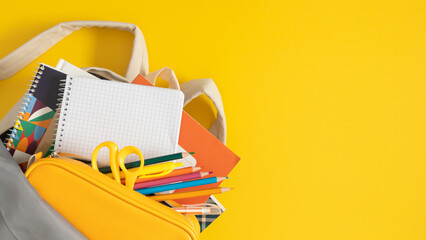 Multicolored school supplies in a beige school backpack, yellow pencil case, pencils, notebooks,...