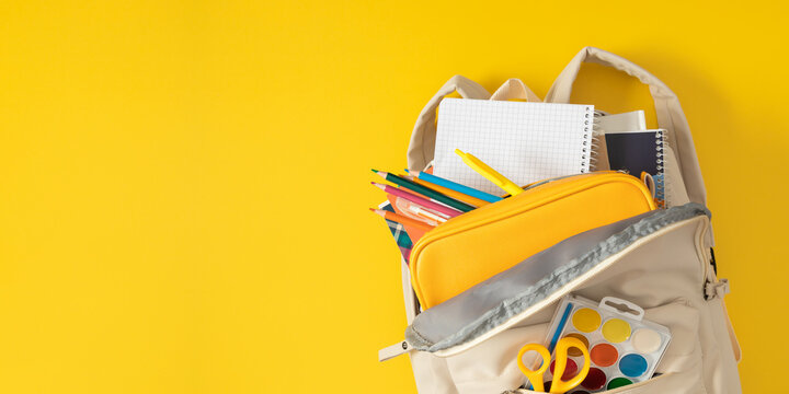 School open backpack filled with colorful school supplies, pencil case, pens, notebooks, pencils, watercolor paints lies on a yellow table background. Back to school banner. - Powered by Adobe