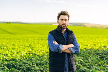 Confident farmer standing with crossed arms in cultivated soybean field during sunset