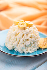 White Сottage cheese, Curd, with Banana on blue wooden and orange textile, side view, close up, selective focus