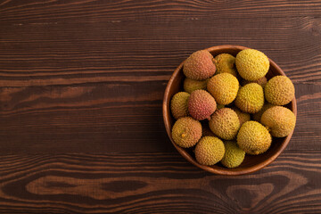 Ripe Lychee on clay bowl on brown wooden, top view, flat lay, copy space, minimalism