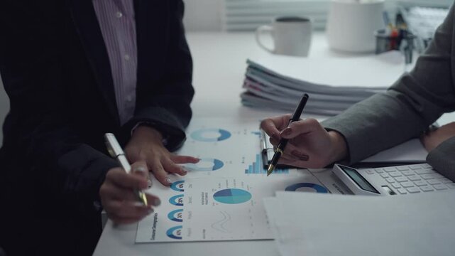 Professional businesswomen analyzing financial reports, collaborating on investment strategies while pointing at charts in modern office setting