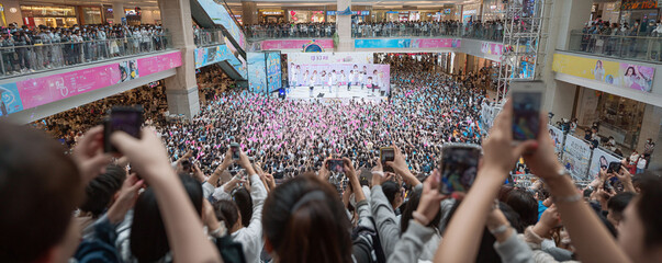 A sea of fans at a live concert in a shopping mall, capturing the event with their phones. Demonstrates excitement, connection, and the power of live entertainment.