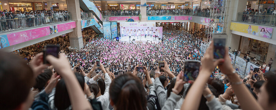 A sea of fans at a live concert in a shopping mall, capturing the event with their phones. Demonstrates excitement, connection, and the power of live entertainment.