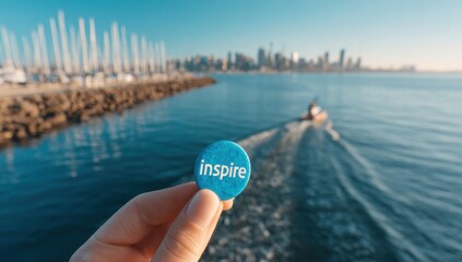 Inspire" button held over the ocean, with blurred skyline and boat. Serene blue water contrasts with the motivational message. Coastal vista; blurred boat on the right