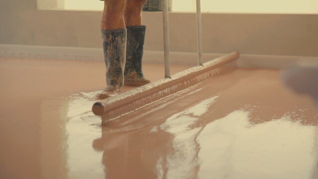 Construction worker leveling self-leveling anhydrite gypsum screed with rake