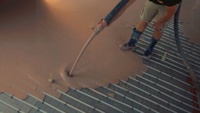 Construction worker pouring self-leveling anhydrite gypsum screed on underfloor heating system