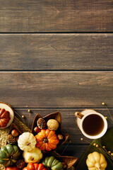 Warm autumn flat lay with cup of tea on green cloth, colorful mini pumpkins, pine cones, nuts, and acorns arranged around a leaf-shaped wooden tray on rustic wood