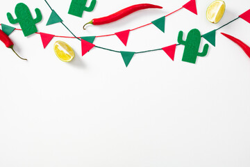 Festive flat lay with red chili peppers, lemon halves, felt cacti, and colorful pennant flags on white. Mexican holidays celebration banner design