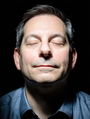Obraz premium A close-up portrait of a middle-aged man with eyes closed, appearing calm and content against a dark background.
