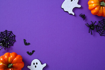 Purple Halloween background with pumpkins, bats, ghosts, spiders, and webs arranged in a creative...