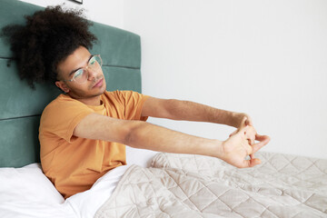 Side view horizontal image of lazy man of african ethnicity in bed, stretching hands and body,...