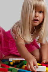 blonde blue-eyed girl, 4 years old, playing with a construction set at home