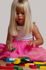 blonde blue-eyed girl, 4 years old, playing with a construction set at home