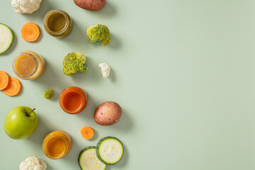 Assorted fresh vegetables and baby food jars on a light green surface. Includes broccoli, cauliflower, carrots, zucchini, potatoes, and apple. Ideal for healthy baby nutrition themes.