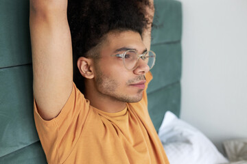 Closeup side view of dark-skinned male bachelor with afro hair in pajama raising hands up sitting...