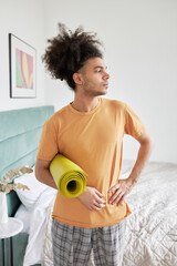 Vertical indoor image of youthful athletic african american guy with afro hair holding rolled...
