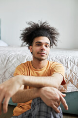 Relaxed smiling african american z-generation boy with funny hairstyle having rest sitting on floor next to bedroom after cleaning apartment and doing household chores on sunday morning