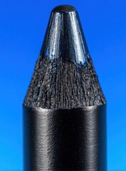 Sharpened black pencil, close up view against a gradient blue background showcasing the textured graphite core, smooth shaft, and fine detailing
