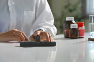 Close up of person organizing daily medication on desk. Health and medication concept