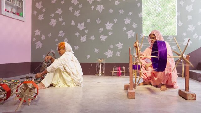 Two women work with handlooms and spinning wheels to wind colourful thread in a traditional Indian home. A scene of rural India&rsquo;s textile craftsmanship and handmade weaving.