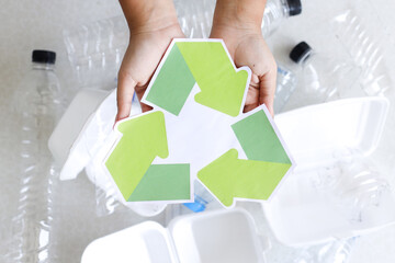 Overhead View Of Hands Showing Recycling Symbol Over Discarded Plastic Bottles And Containers