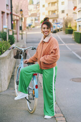 Outdoor fashion portrait of pretty african woman walking with bicycle 
